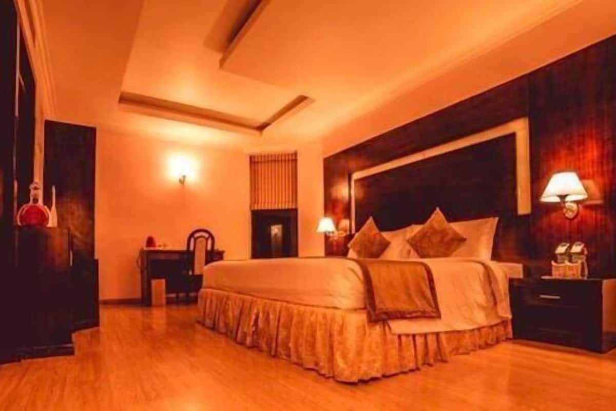 Una habitación de hotel con una cama grande, lámparas de noche, una mesita de noche, un escritorio y una silla.