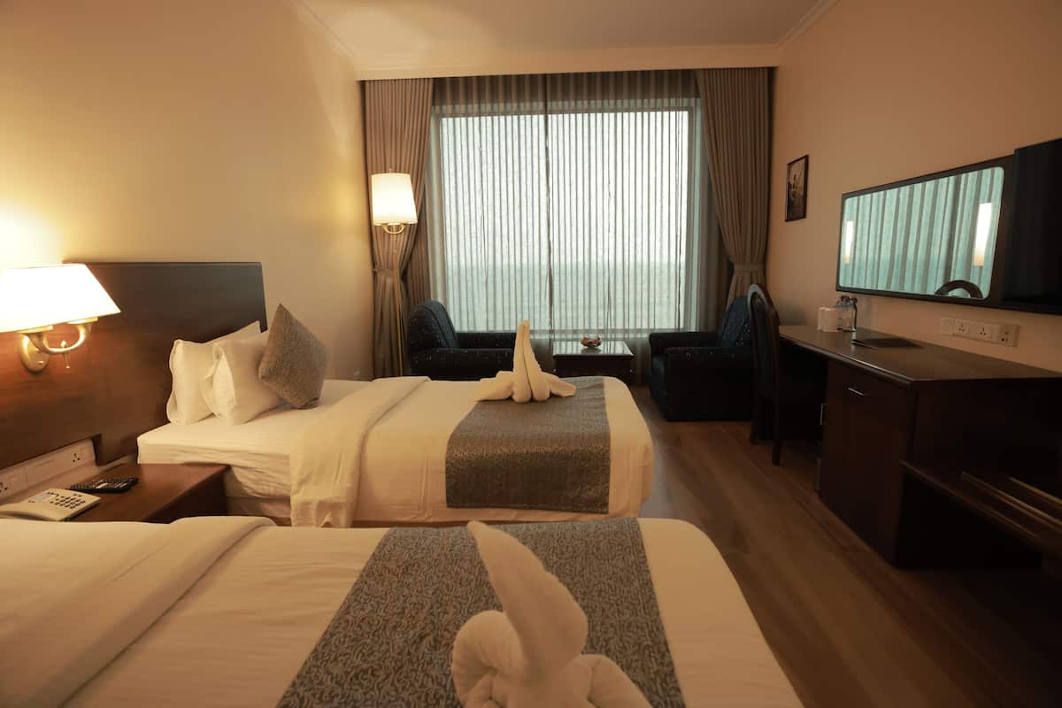Habitación de hotel con dos camas, un escritorio con silla, un televisor y una ventana con cortinas.