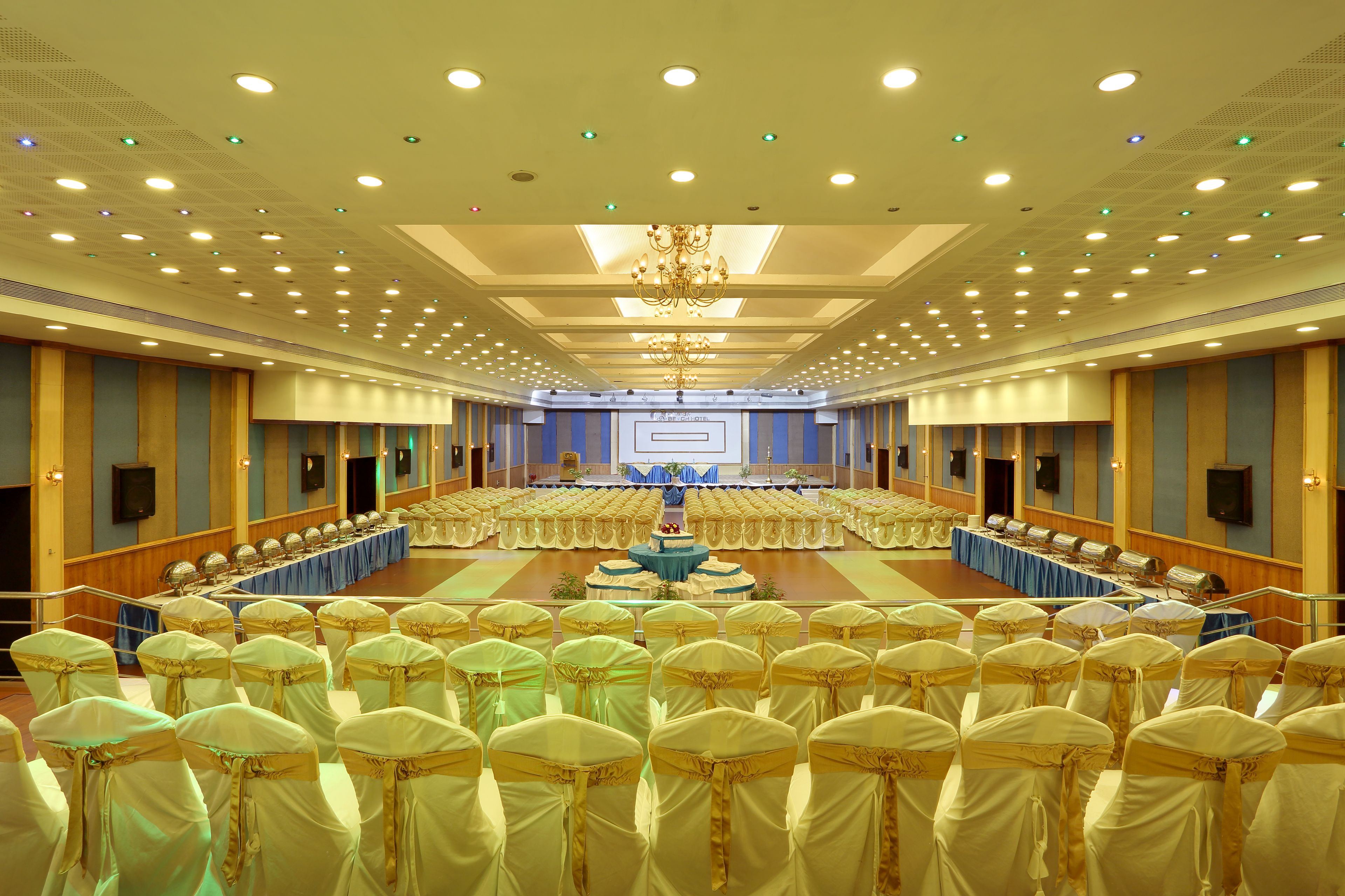 A large conference room with rows of chairs, a stage with a podium, and a chandelier.