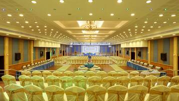 A large conference room with rows of chairs, a stage with a podium, and a chandelier.