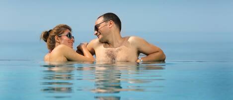 A couple in a clear blue infinity pool with a view of the ocean.
