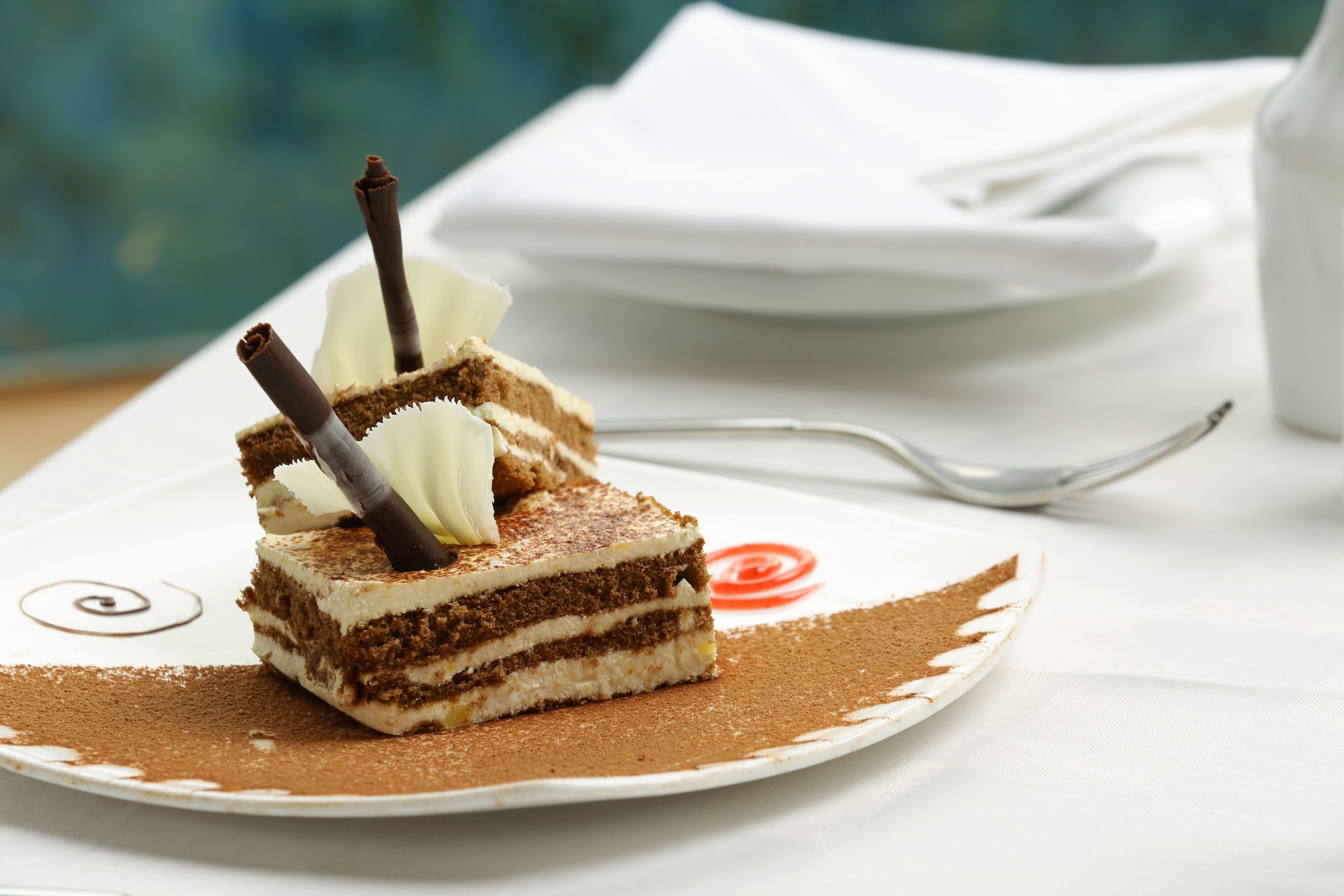 Une part de gâteau à plusieurs couches, décorée de bâtonnets de chocolat, est présentée sur une assiette. Une serviette et une cuillère sont posées à l'arrière-plan.