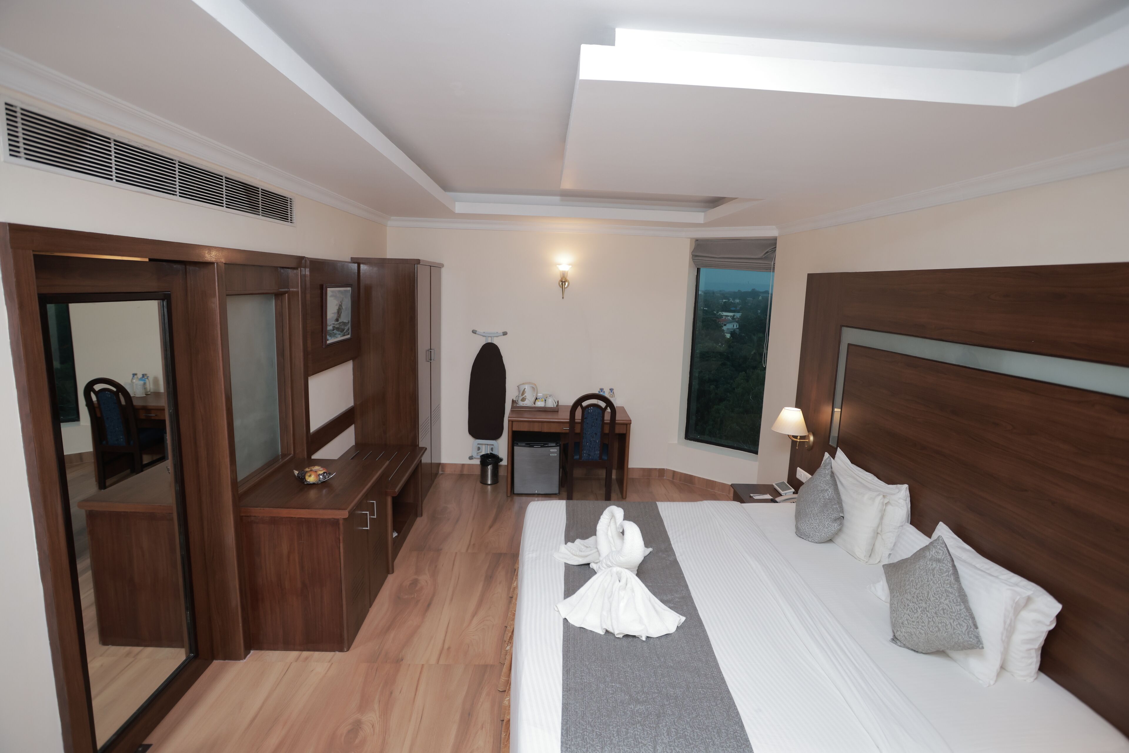 A hotel room with a bed, a desk, a chair, a wardrobe, and a large window.