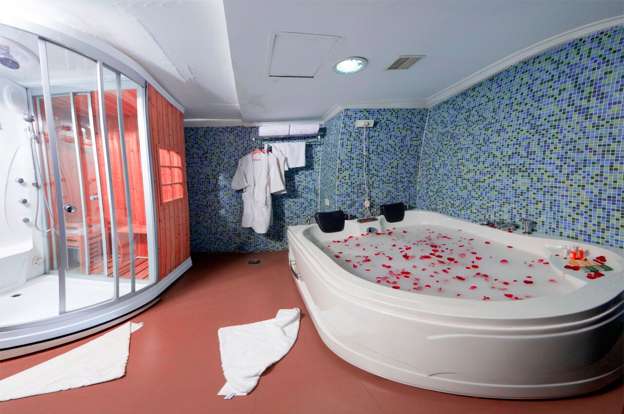 Une salle de bain dotée d’une grande baignoire remplie de pétales de roses, d’une douche en verre et d’un mur carrelé.