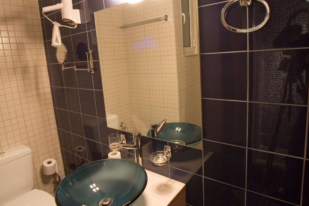 A bathroom with a toilet, a sink with a glass basin, a mirror, and a towel rack.