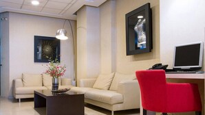 A modern living room with a beige sofa, a red chair, a coffee table with a vase of flowers, a desk with a computer, and artwork on the walls. - Olympic Star (Patras)