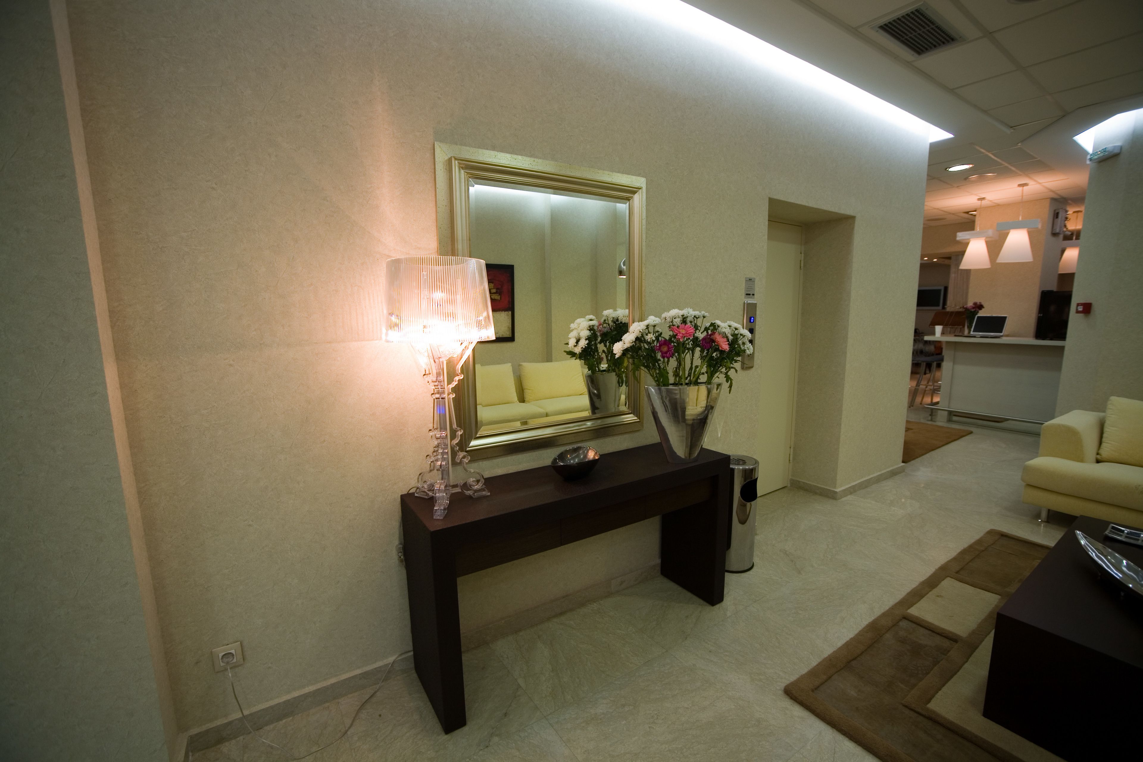 A reception area with a dark console table, a mirror, a lamp, and a vase with flowers.