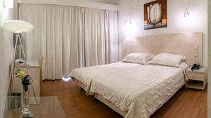 A bedroom with a large bed, a bedside table with a lamp, a nightstand with a phone, and a painting on the wall. - Olympic Star (Patras)
