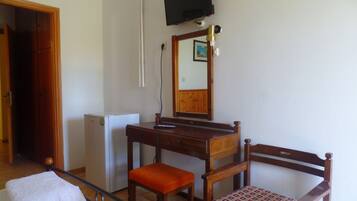 A room with a wooden desk, a chair, a bed, a TV mounted on the wall, and a small refrigerator.