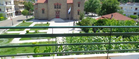 A stone church with a bell tower, surrounded by greenery and modern buildings.