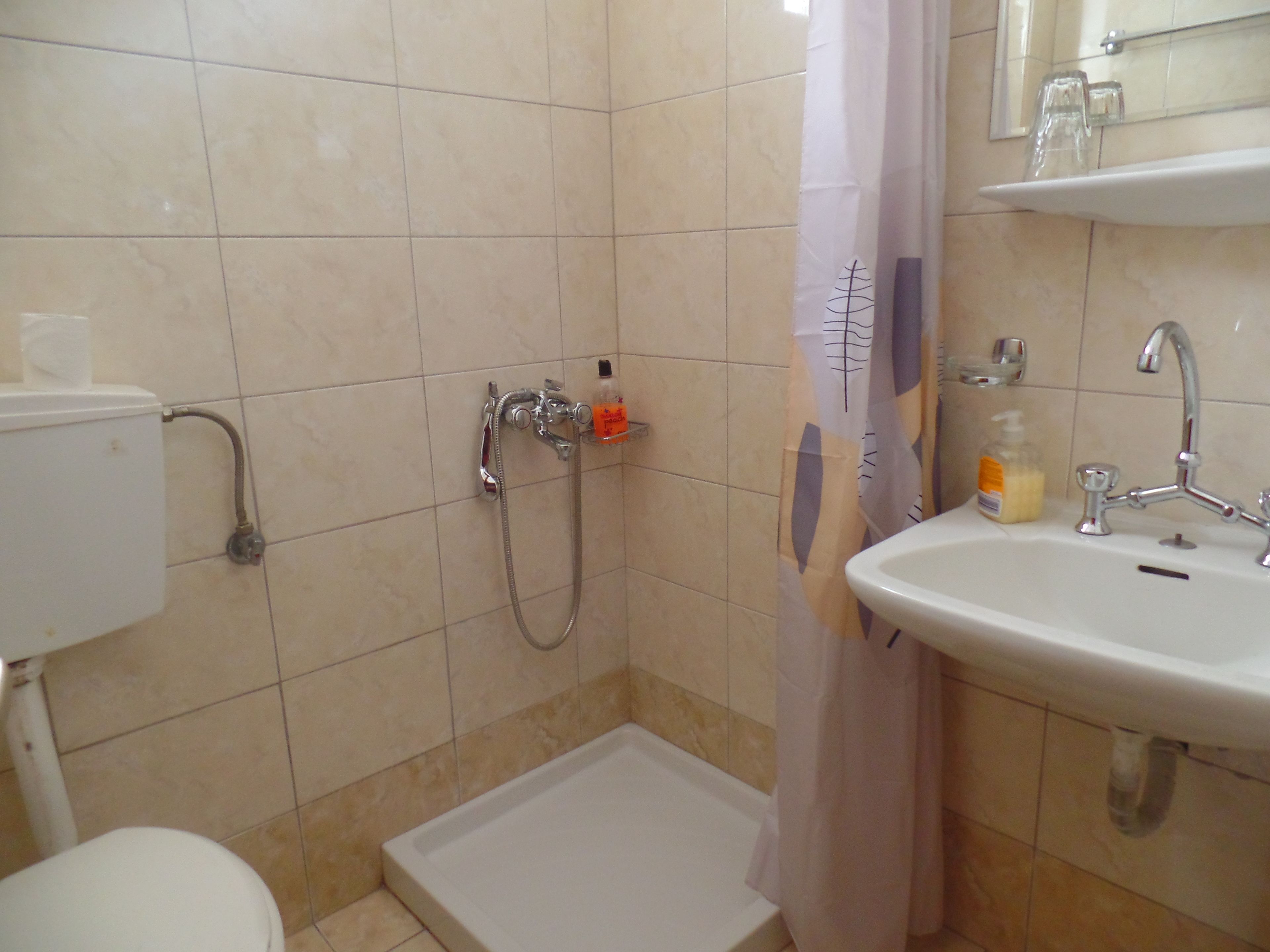 Un baño con ducha, inodoro, lavamanos y puerta de vidrio para la ducha.