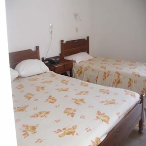 Ein Zimmer mit zwei Einzelbetten, beide mit einem Holzkopfteil und einer floralen Bettdecke. Ein Nachttisch mit Telefon und eine Steckdose sind an der Wand angebracht.