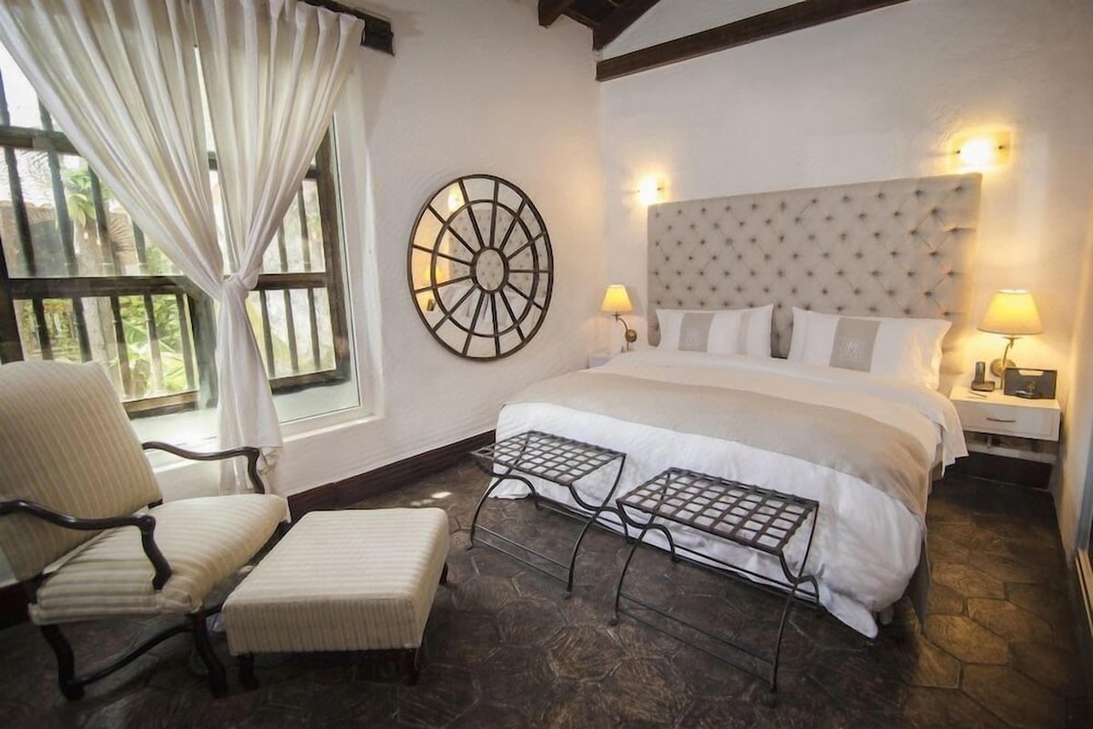 Un dormitorio con una cama grande, una silla, una mesita y un adorno en la pared.