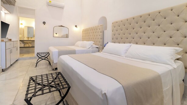 Une chambre d’hôtel avec deux lits, une grande tête de lit capitonnée, une petite table, un miroir et une armoire.