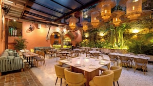 Restaurante com mesas e cadeiras de madeira ao ar livre, cercado por um muro de pedra e vegetação.