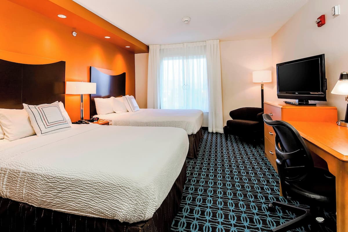 A hotel room with two beds, a desk with a TV, and a patterned carpet.
