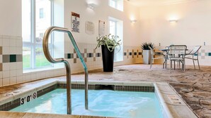 Zona de piscina con letrero de límite de profundidad de 3 pies, aviso de socorrista de servicio y área de descanso con sillas y una mesa.
