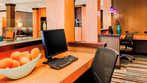 Un mostrador de recepción de hotel con una computadora, un cuenco de naranjas y un jarrón con flores secas.