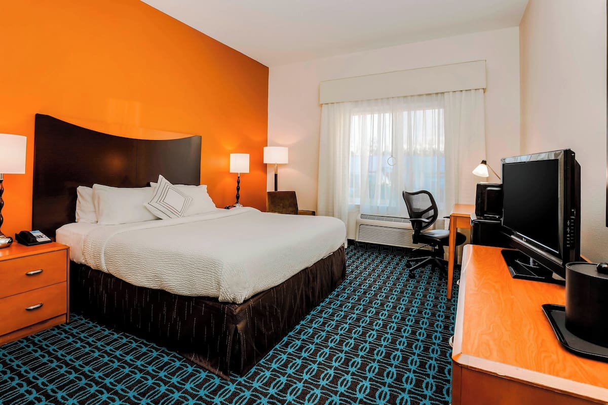 A hotel room with a large bed, two bedside lamps, a desk with a computer, and a television.
