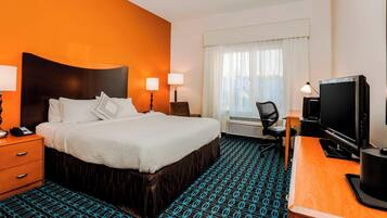 A hotel room with a large bed, two bedside lamps, a desk with a computer, and a television.