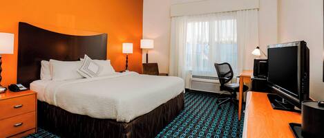 A hotel room with a large bed, two bedside lamps, a desk with a computer, and a television.
