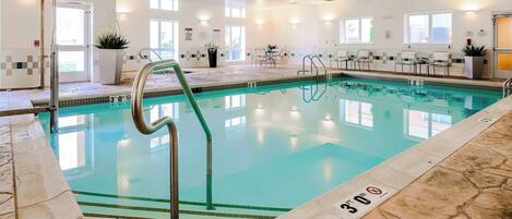 Una piscina interior con agua cristalina, una silla de salvavidas y un solárium con baldosas.