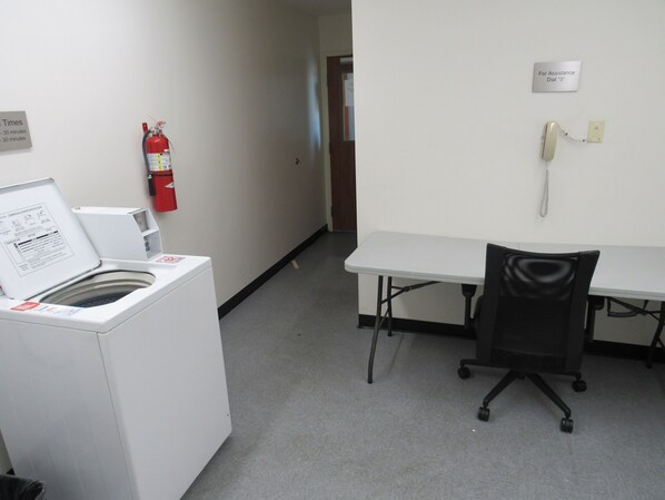 A small office with a white desk, a chair, a fire extinguisher, and a telephone.