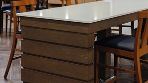 Un comedor moderno con una larga mesa rectangular, sillas de madera y una cocina al fondo.