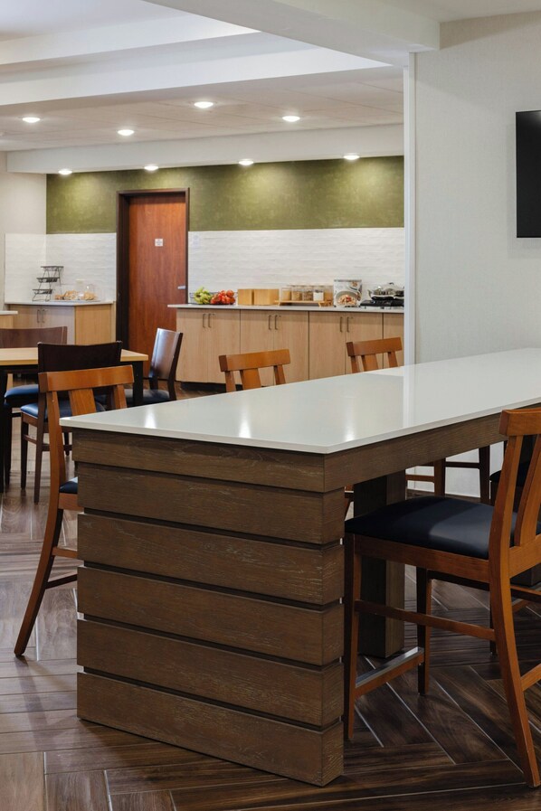 A modern dining area with a long rectangular table, wooden chairs, and a kitchen in the background. - Fairfield Inn & Suites by Marriott Fort Wayne (Fort Wayne)