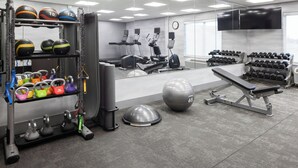 Un gimnasio con cintas de correr, elípticas, una banca, una pelota medicinal y diferentes pesas.