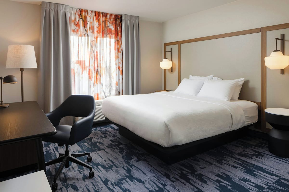 Una habitación de hotel con una cama grande, un escritorio, una silla y una ventana con cortinas.