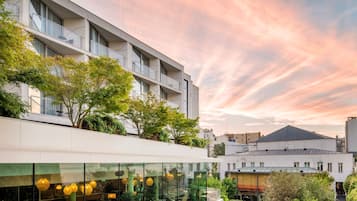A modern building with a glass facade, outdoor seating area, and a rooftop garden.