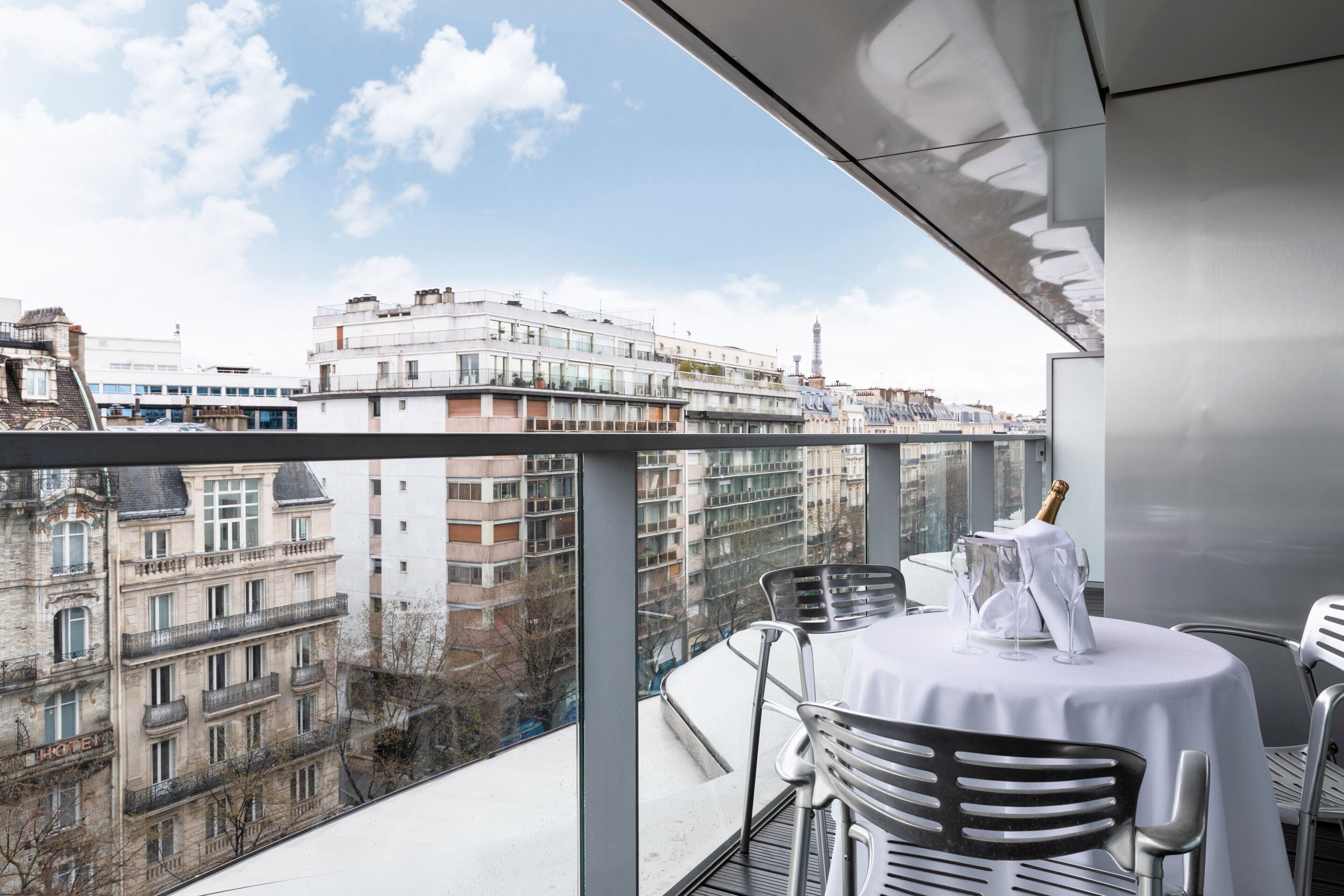 Een balkon met een tafel gedekt voor twee, met uitzicht op een stadsgezicht met historische gebouwen en een toren in de verte.