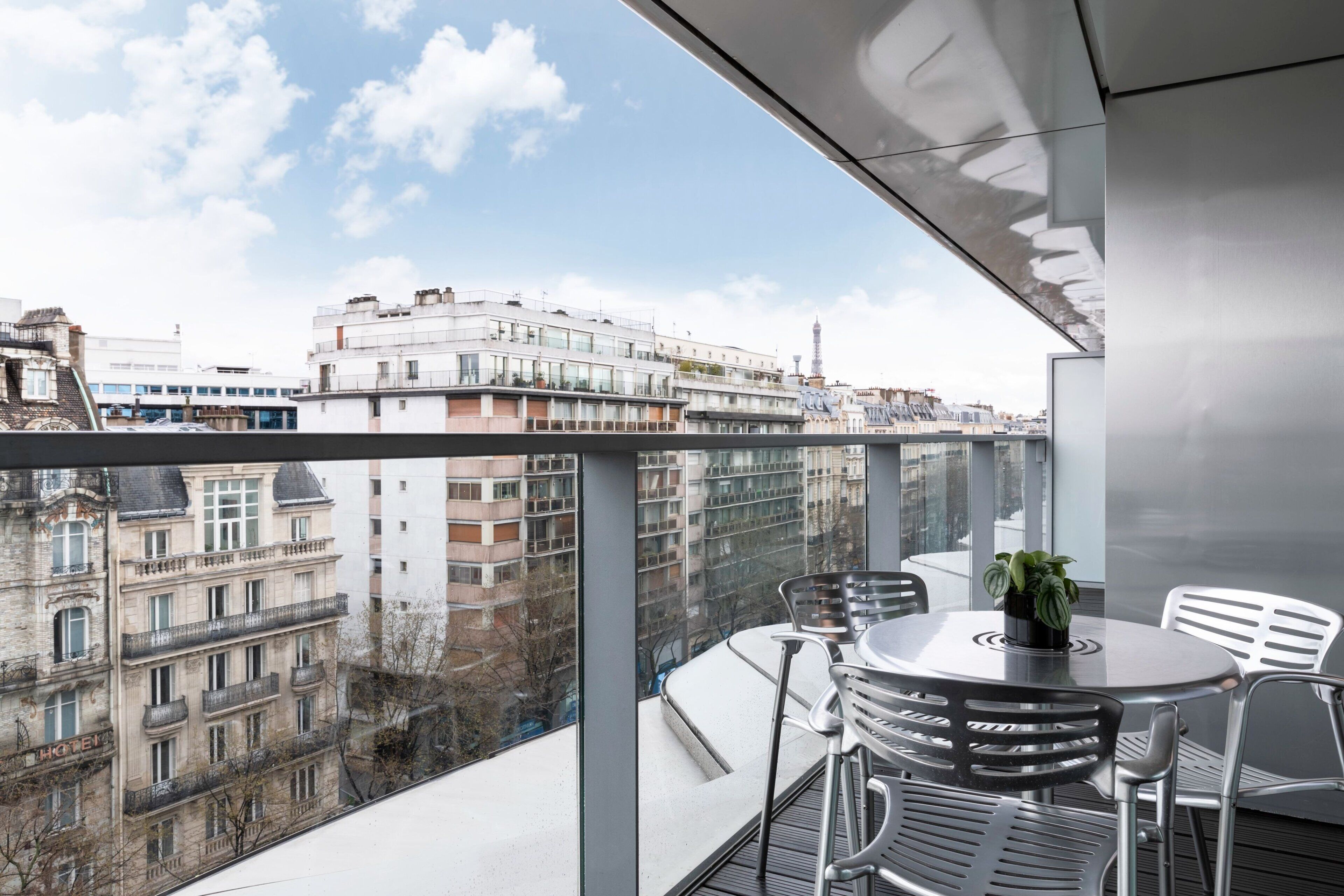 A balcony with a table and chairs, a potted plant, and a view of city buildings.