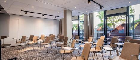 A conference room with rows of chairs and tables, large windows with curtains, and a ceiling with recessed lighting.