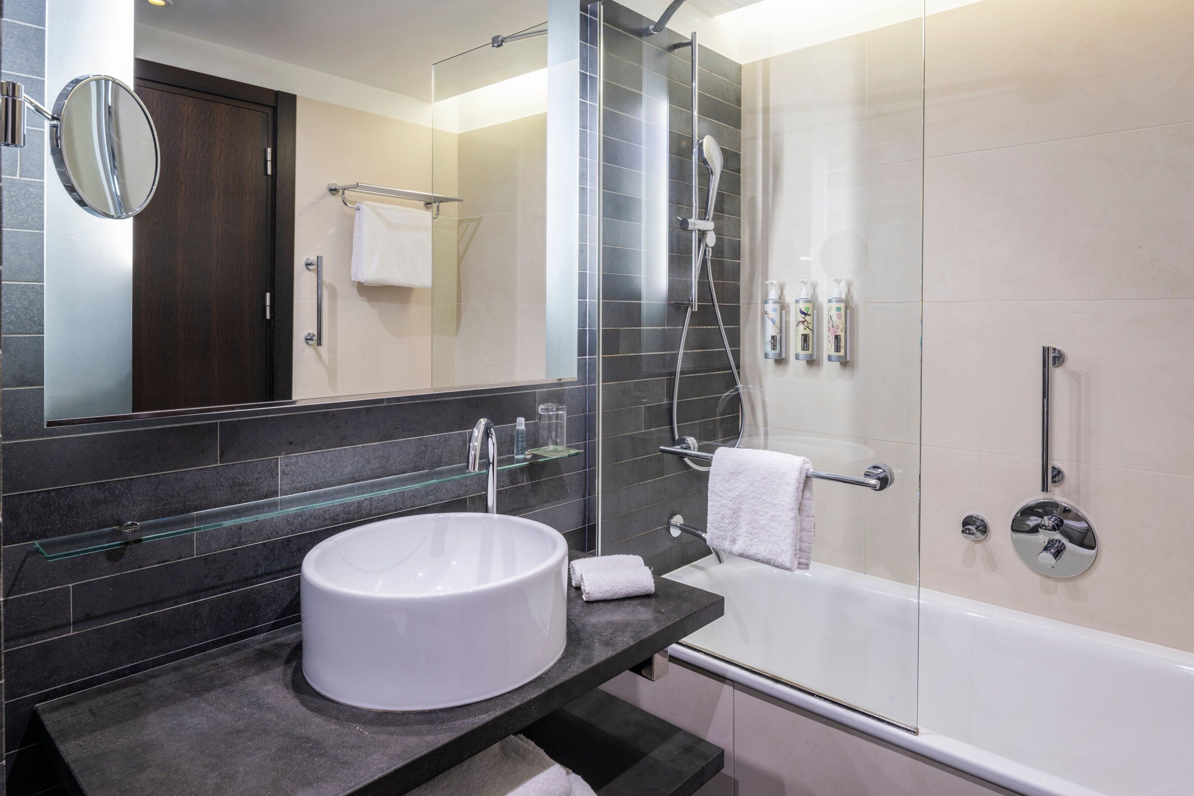 A modern bathroom with a round white sink, a glass-enclosed shower, and a large mirror.