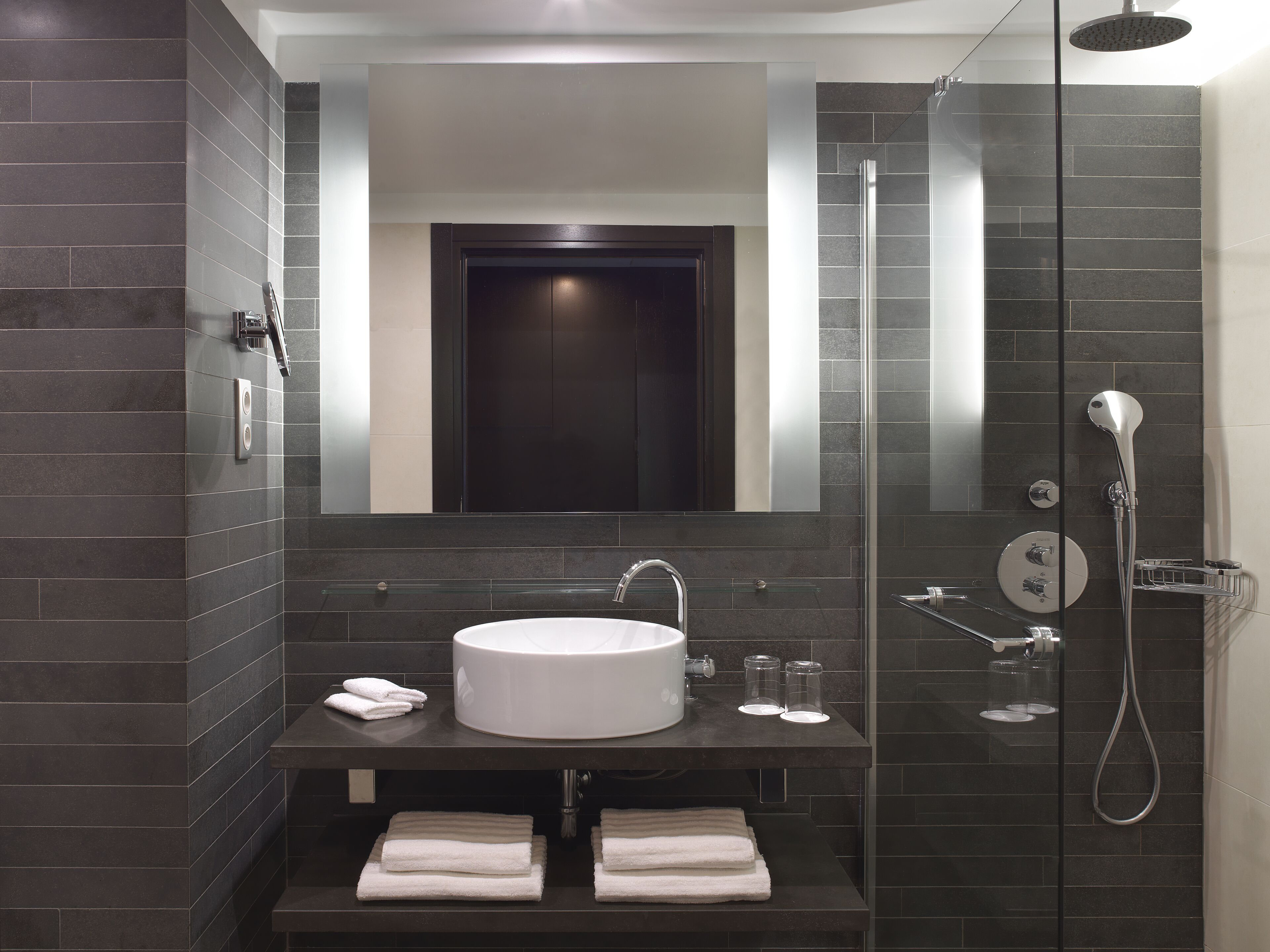 A modern bathroom with a large mirror, a round sink, and a glass-enclosed shower area.