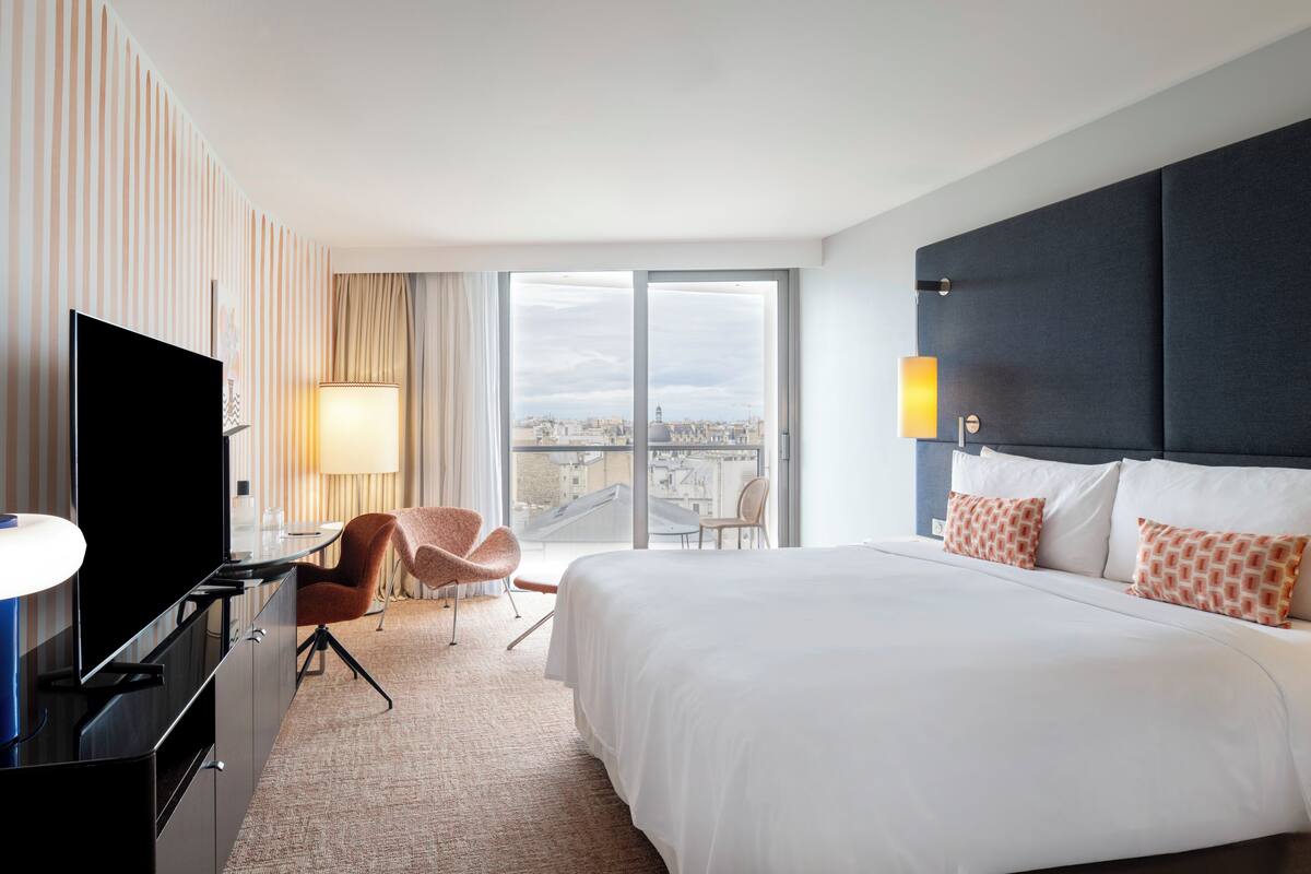 Une chambre d’hôtel avec un grand lit, une télévision, une chaise, un bureau et une vue sur la ville.