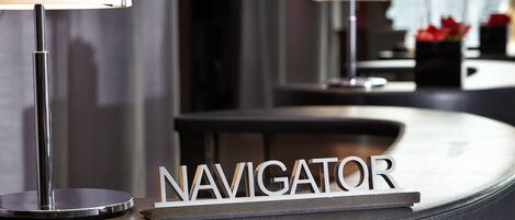 Un mostrador de recepción con un letrero que dice "NAVIGATOR" y una lámpara a la izquierda.