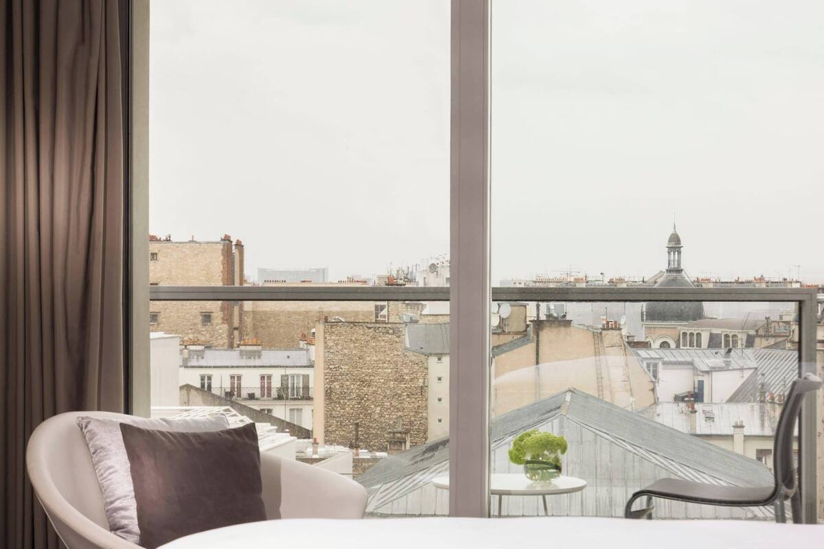 Une chambre d’hôtel moderne dotée d’une grande fenêtre donnant sur le paysage urbain, avec notamment une vue sur une tour imposante.