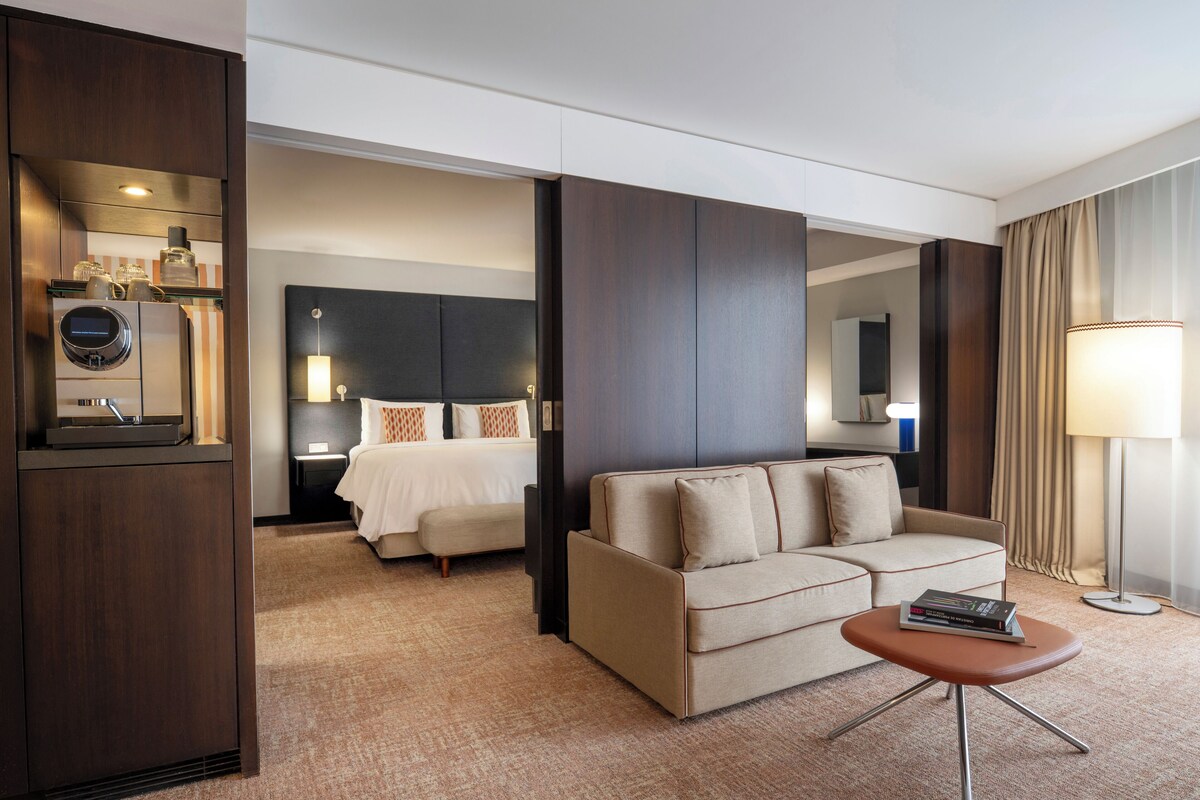 Une chambre d’hôtel avec un lit, un canapé, une petite table, une lampe et un miroir.