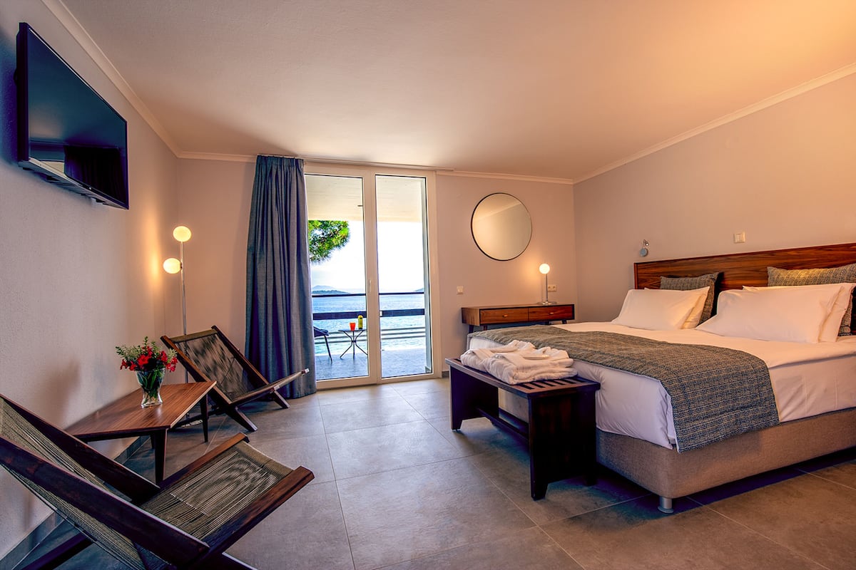 Habitación de hotel con cama, escritorio con silla, televisor montado en la pared y vistas al exterior a través de una puerta corrediza.