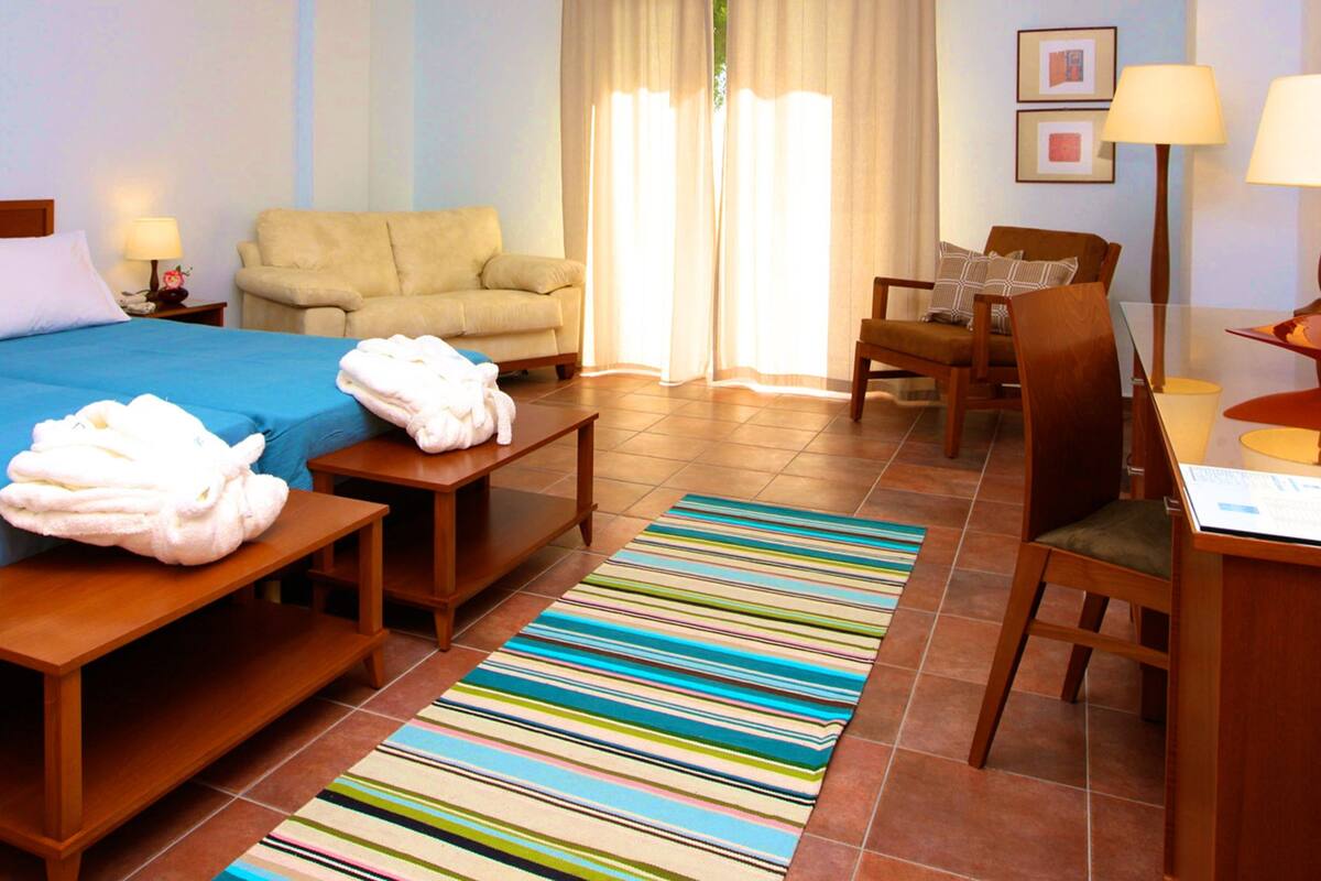 Habitación de hotel con cama, una silla, escritorio y ventana con cortinas.