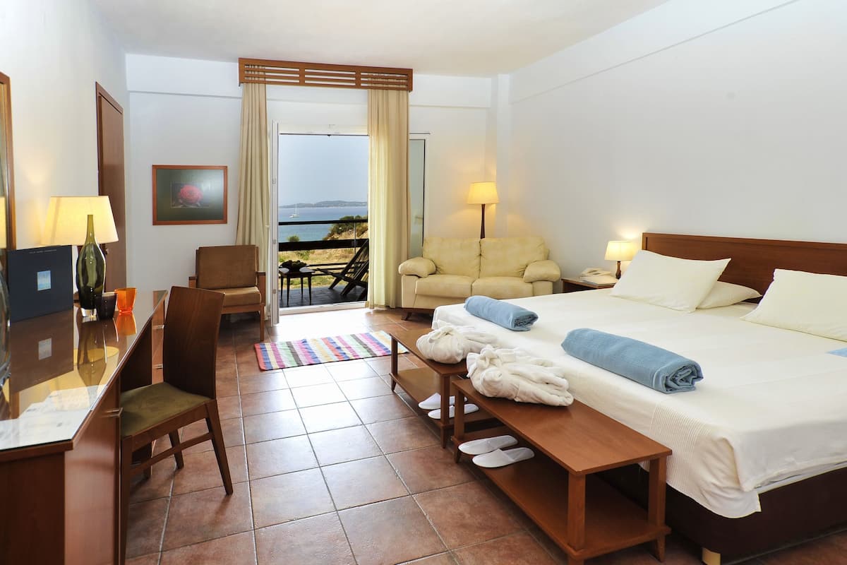 Habitación de hotel con cama, escritorio, silla, sofá, televisor y vista al mar.