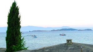 A stone building with a sloped roof overlooking a body of water with boats. - Xenia (Aristotelis)