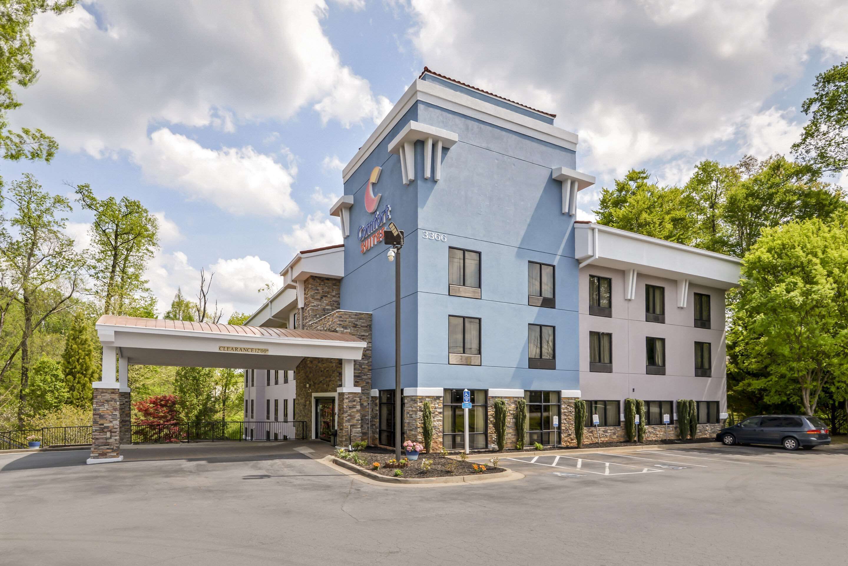 A hotel with a blue and white exterior, a covered entrance, and a parking lot.