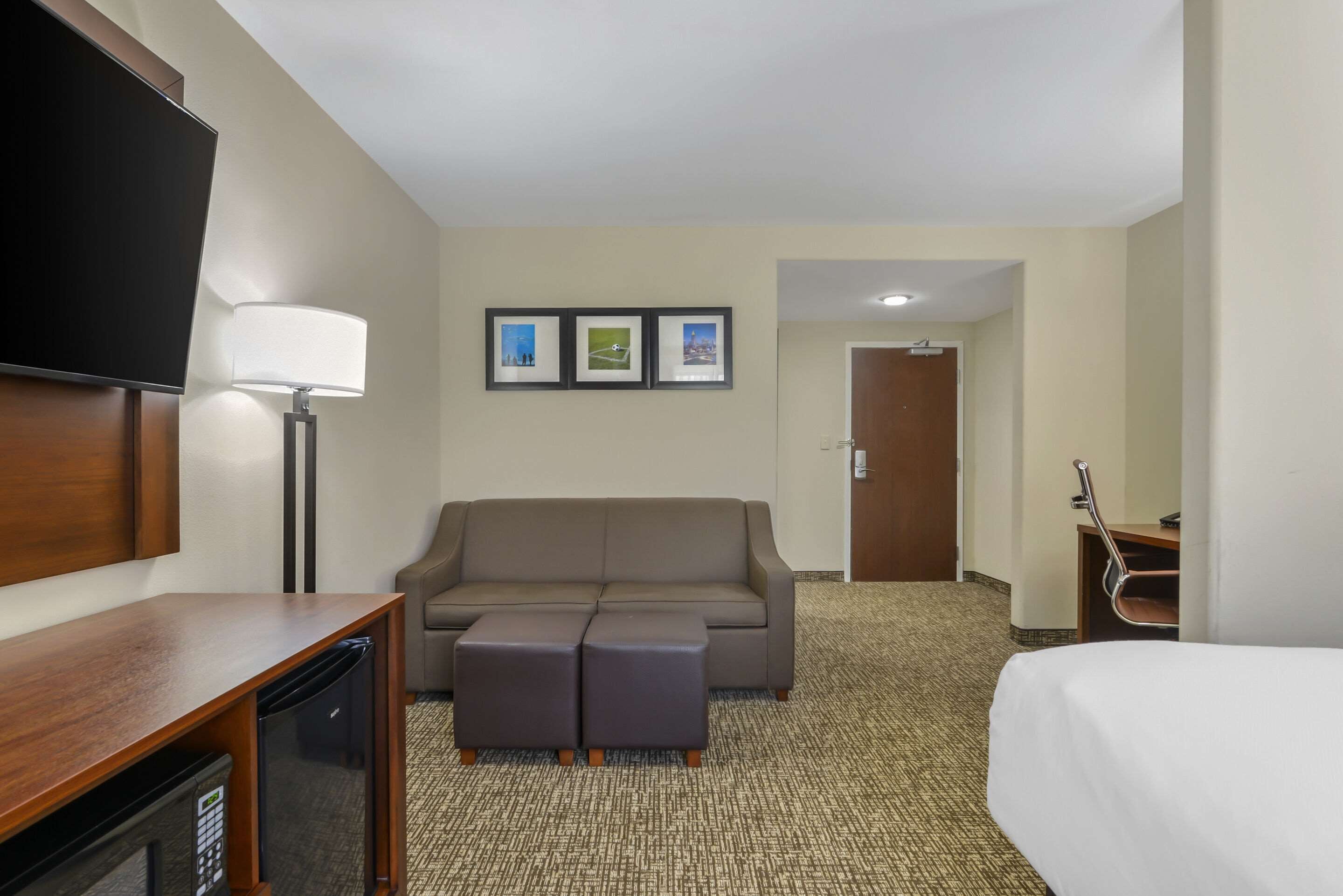 Ein Hotelzimmer mit einer Couch, einem Fernseher, einer Lampe, einem Schreibtisch mit eingebauter Mikrowelle und einem Bett.