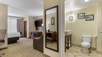 A hotel room with a bed, desk, chair, TV, and a bathroom with a toilet and sink.