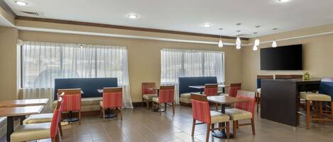 A dining area with booths and tables, large windows with curtains, and a flat-screen TV mounted on the wall.