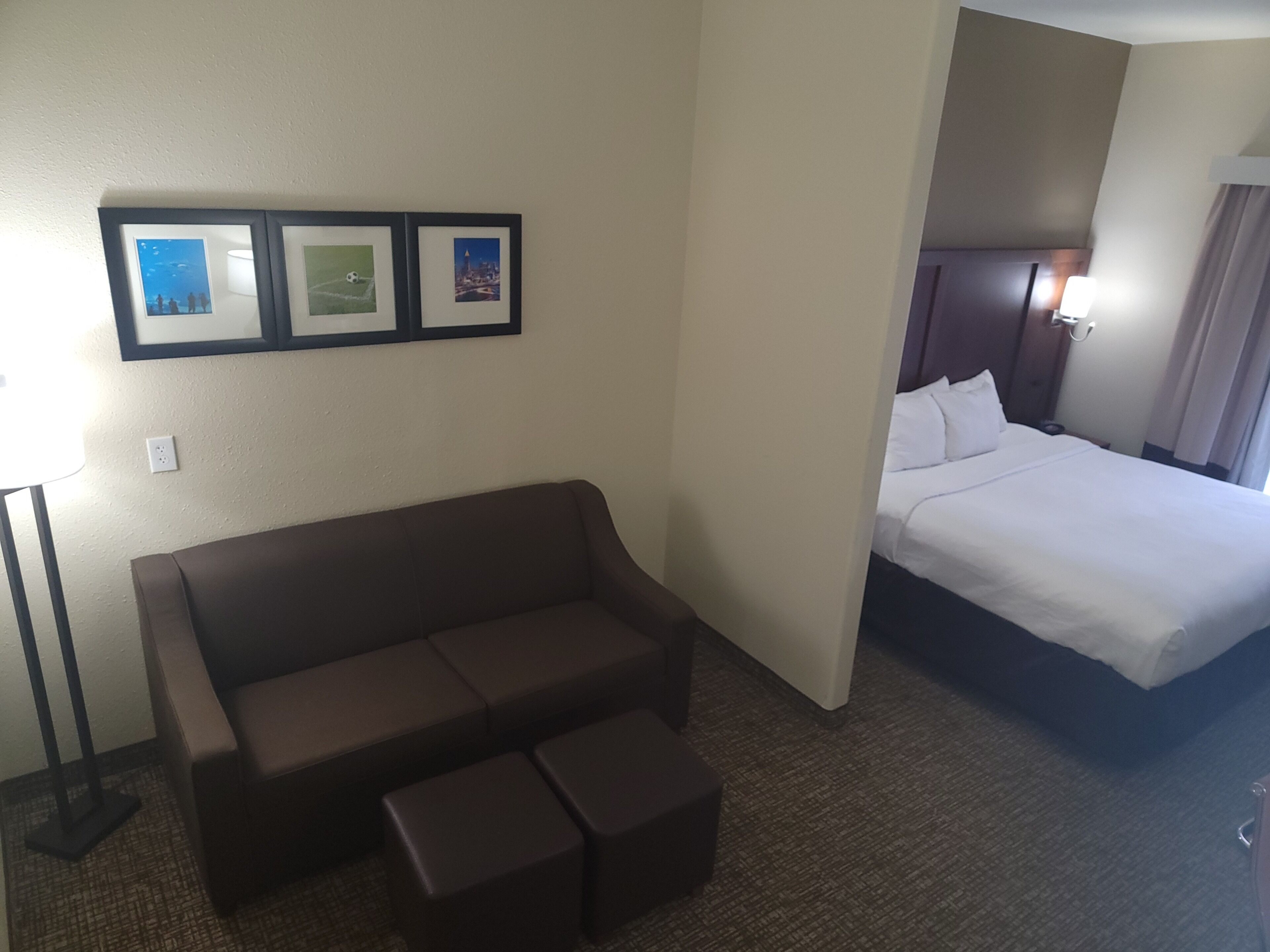 A hotel room with a brown sofa, a bed, and three framed pictures on the wall.